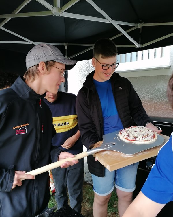 Zwei jungen die mit einem Pizzaschieber eine rohe Pizza von einem Brettchen aufnehmen | © RÖSLE GROUP Zwei jungen die mit einem Pizzaschieber eine rohe Pizza von einem Brettchen aufnehmen | © RÖSLE GROUP