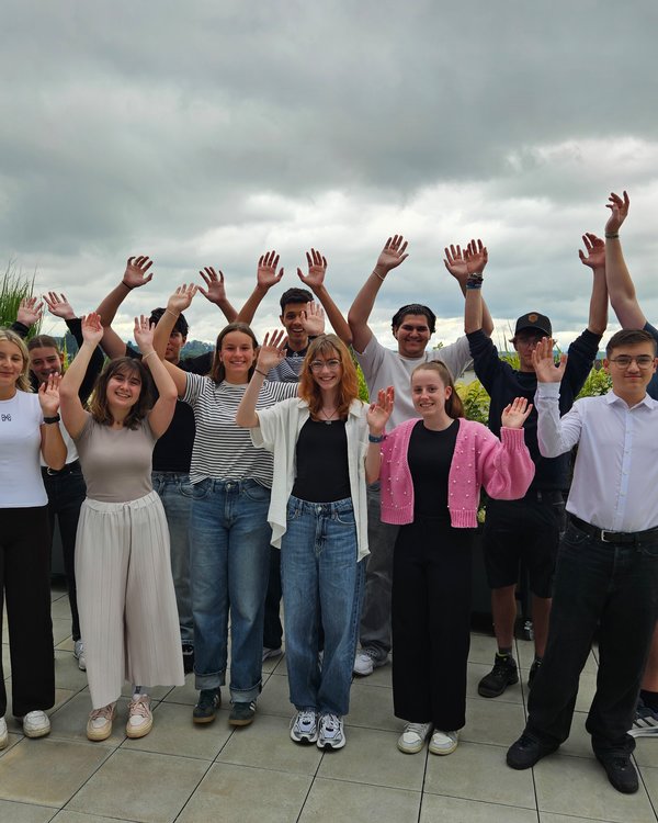Grillschulung 2025 | © RÖSLE GROUP 13 junge Menschen stehen auf einer Dachterasse und heben in die Hände hoch. Alle lächeln in die Kamera | © RÖSLE GROUP