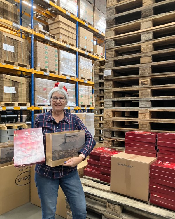 Eine ältere Frau hat eine Weihnachtsmütze auf den Kopf und hält einen Adventskalender und eine Tüte in der Hand | © RÖSLE GROUP