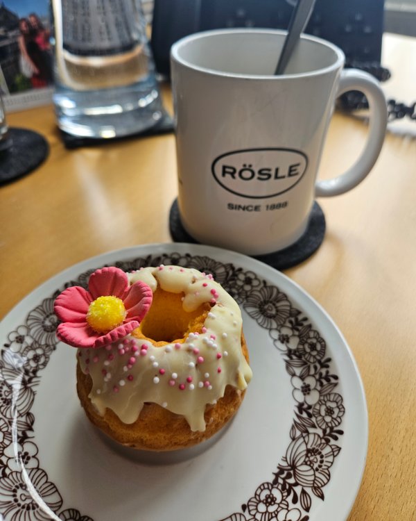 Ein kleiner Kuchen der schön mit vielen Farben varziert ist steht auf einem Teller. Im Hintergrund kann man eine Tasse sehen auf der "Rösle" steht | © RÖSLE GROUP